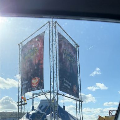 Zwei große Werbebanner auf einem Gestell, im Freien, bei sonnigem Wetter.