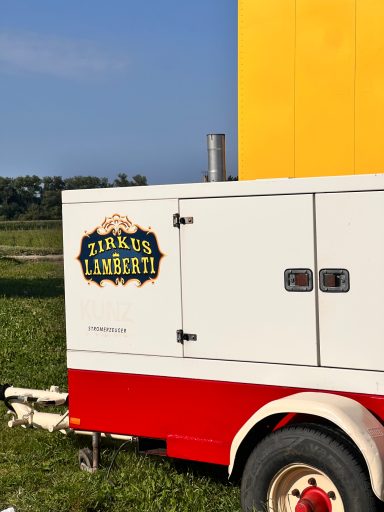 Fahrzeug mit buntem Logo und Anhänger in einer grünen Wiesenlandschaft.